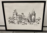 Framed monochrome print of Casa Loma by Al. J. Casson signed in pencil and dated 1977, shown hanging and angled views.