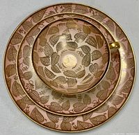 Top view of the cup placed inside the saucer, both resting on the plate, showing intricate gold leaf pattern and gold trim on pink background