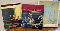 Three art books arranged standing and leaning: 'Hopper', 'American Realism', and 'Picasso in Montreal'