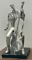 Front view of silvered metal jazz musician figure seated playing double bass on black base