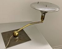 Side angle showing curved brass arm, square metal base, and aluminum flying saucer shade with screws on top.