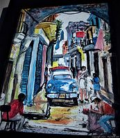 Close-up of oil painting showing Cuban street scene with vintage blue car and figures in colorful buildings, mounted in a black wood frame.