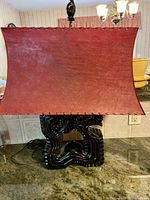 Front view of Asian inspired dragon table lamp, showing red curved rectangular fabric lampshade and glossy black dragon-shaped ceramic base on a counter.