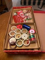 Top view of a box with multiple ribbon spools and gift bows, some ornaments and tags visible