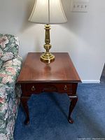 Front view of the cherry wood end table along with the brass lamp on top, showing the overall design, condition, and style beside floral couch.