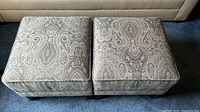 Two square hassocks upholstered in paisley pattern fabric, placed side by side on carpet.
