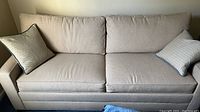 Front view of the Ethan Allen beige upholstered queen size sofa with two matching decorative pillows.