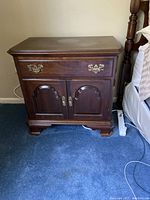 Ethan Allen solid cherry nightstand beside bed showing drawer, cabinet doors, brass hardware, and bracket feet.