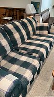 Photo showing large green and off-white plaid sofa with cushion on carpeted floor, angled view of left side arm and back