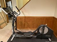 Side view of elliptical machine showing frame, foot pedals and flywheel housing