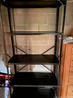 Black metal shelving unit with adjustable shelves against concrete block wall.