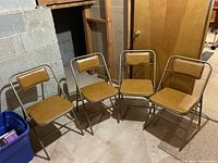 Four mid century modern folding chairs arranged in a row in a basement setting. All chairs have metal frames and brown vinyl padded seats and backs.