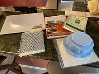 Overview of all items on a kitchen counter including cookbooks, cutting board, pot holder, and china inserts.