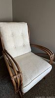 Front angled view of the rattan chair showing seat and back cushions and rattan armrests.