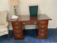 Overall view of solid wood desk with table lamp on top and part of armchair visible