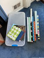 Clear plastic under bed storage container on blue carpet, several small gift bags inside.