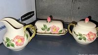 Full view of pitcher, butter dish, and covered pot showing floral decoration and handles