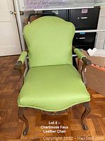 Front view of a restored vintage chair with chartreuse faux leather upholstery, wooden carved legs, padded armrests partially wrapped in matching material, showing seat and backrest