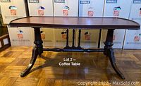 Front view of the antique coffee table showing rectangular top, carved legs, and brass feet.