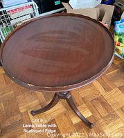 Top view showing round wooden table top with scalloped edge and minor damage at edge.