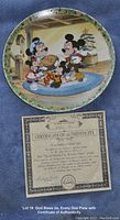 Photo of the decorative plate featuring a Christmas scene with Mickey Mouse and family baking together, alongside the Certificate of Authenticity.
