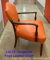 Side view of tangerine faux leather chair showing wooden armrest and leg design.