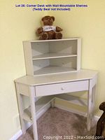 White corner desk positioned in room corner with wall-mounted corner shelf above it. Teddy bear on shelf not included.
