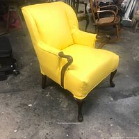 Front view showing bright yellow faux leather upholstery, curved wooden arms, and clawed wooden legs, with slight creasing on the seat.