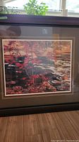 Framed print showing vibrant red maple trees near a flowing river with rocks.