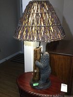 Full view of the bear lamp showing the resin bear climbing a faux tree trunk base with twig lamp shade lit on a wood table.