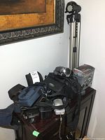 Lot content showing multiple cameras, camera bags, tripod, and boxed flash unit arranged on a small table