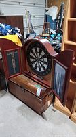 Full view of the vintage wooden dartboard cabinet with doors open revealing the dartboard inside and chalkboard scoring surfaces on the doors.