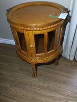 Front view of the wooden drum-shaped display table showing the glass panel doors and claw feet.