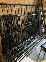 Black metal side rails and support slats for a bunk bed, leaning against a wall in a storage area.