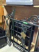Two green metal garden gates with decorative gold flowers and ornate scrollwork resting against a shelf.