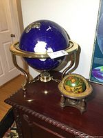 Full view of large dark blue globe in brass frame with smaller vintage globe next to it on wooden surface.