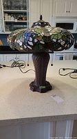 Full view of metal table lamp with stained glass shade on kitchen countertop with pull chains visible.