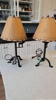 Pair of matching metal table lamps with tan stitched lampshades displaying moose silhouettes on the body, unlit on a white countertop.