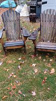 Front view showing pair of brown Adirondack Muskoka chairs on grassy ground with fallen leaves.