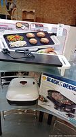 Photo showing Toastmaster Cool-Edge Grill with box and grill surface, also Black & Decker Deep Dutch Electric Skillet in foreground with box.