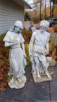 Front view of two large resin statues outdoors, a man with dog and a woman holding a bird.