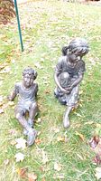 Both statues of boy and girl seated on grass outdoors, showing full figures and condition