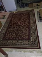Full view of the dark red area rug with beige and gold floral and scroll pattern on floor.