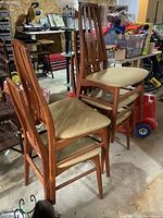 Three teak dining chairs with upholstered seats in storage area