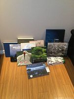Full view of all 10 large hardcover books arranged on the floor, shows various titles and covers including birds, travel, atlas, and art.