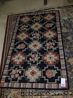 Full view of rectangular vintage hooked rug showing geometric shapes and floral clusters with multicolored striped border.