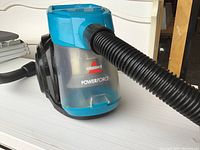 Close-up view of the Bissell Powerforce canister vacuum showing the translucent blue dust container and the attached black flexible hose.