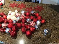 Collection of assorted red, white, and silver Christmas ball ornaments and red snowflake felt decorations on granite countertop.