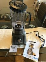 Front view of assembled blender on table with user manual beside it, showing blender base with rotary dial and plastic carafe with lid.