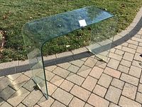 Angled view of clear bent glass occasional table outdoors on paver driveway